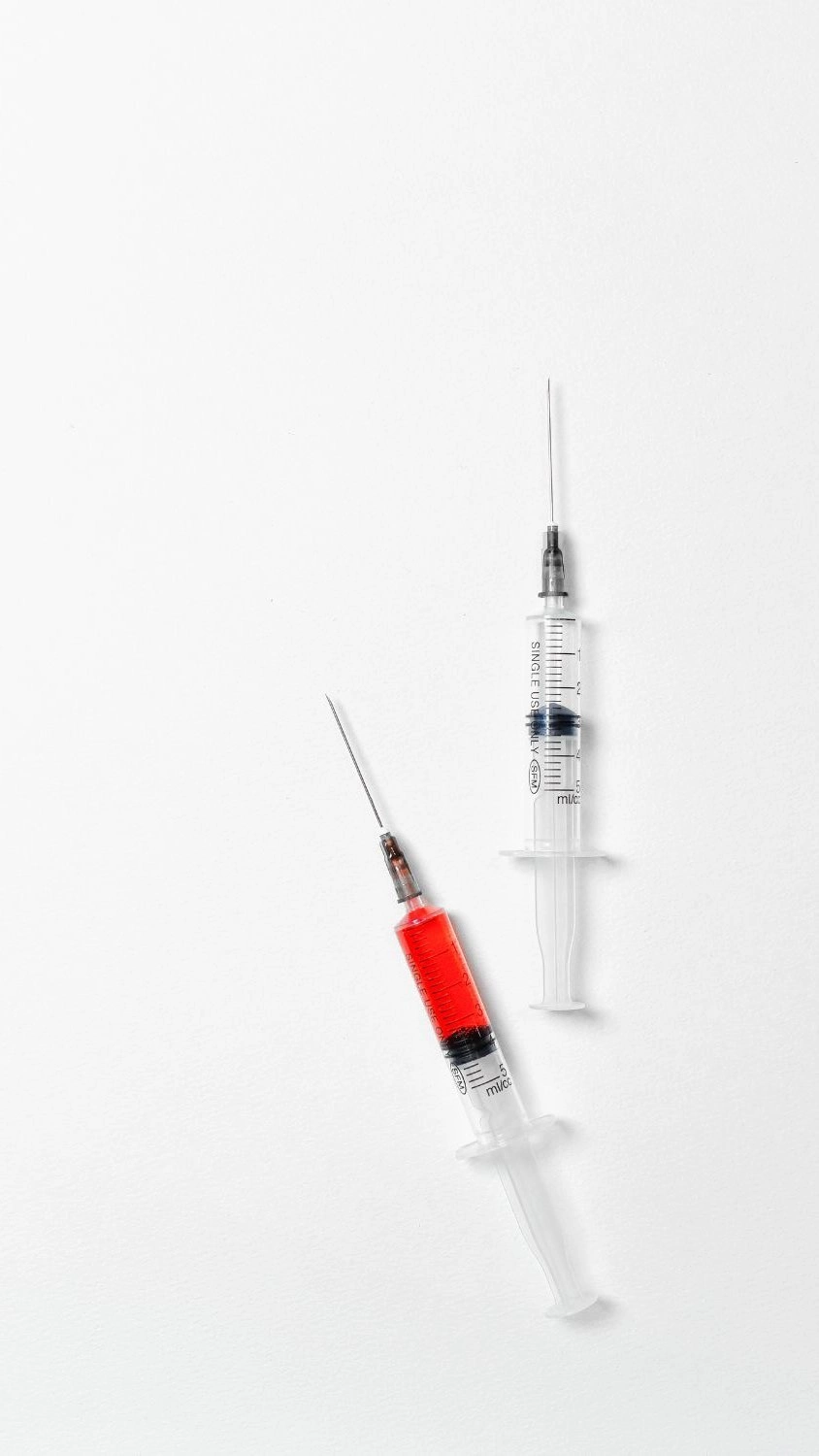 Two medical syringes on a white background, one filled with red liquid.