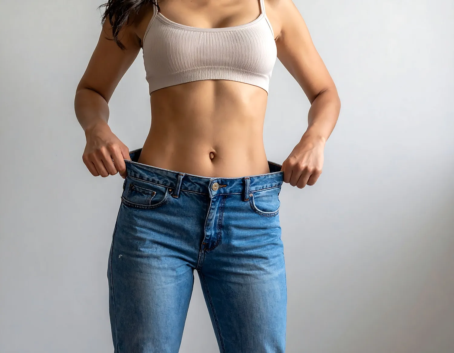 Woman showing weight loss by holding up her loose jeans.