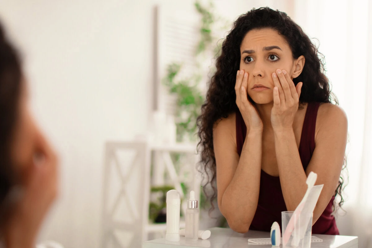 Woman looking into a mirror and touching her face with a concerned expression.