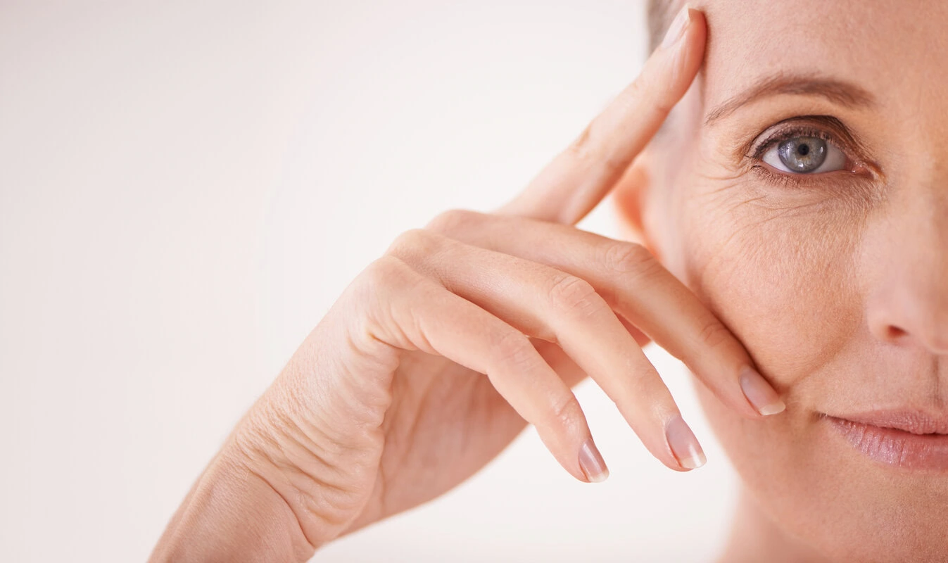 Close-up of a mature woman touching her face near her eye, highlighting skin texture and aging.