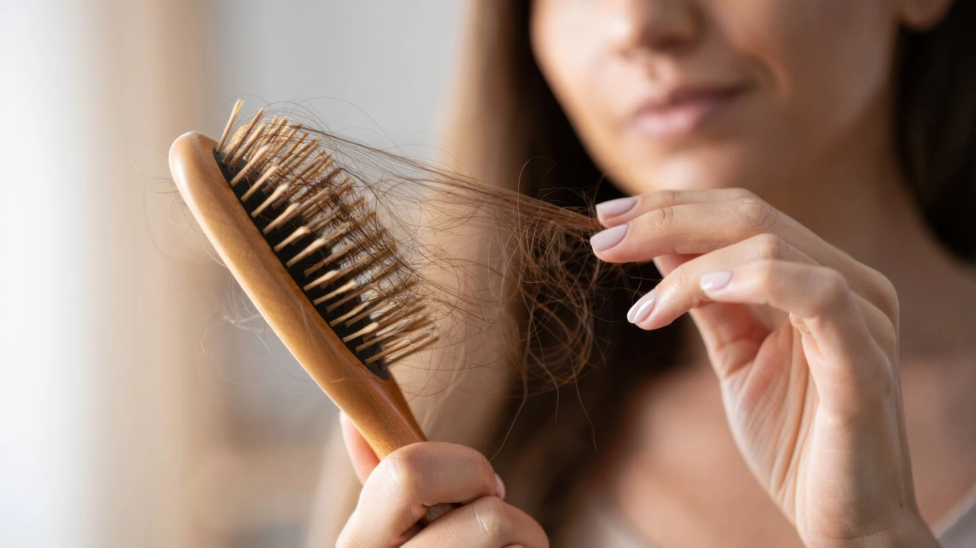Woman holding a wooden hairbrush with a significant amount of fallen hair tangled in the bristles.