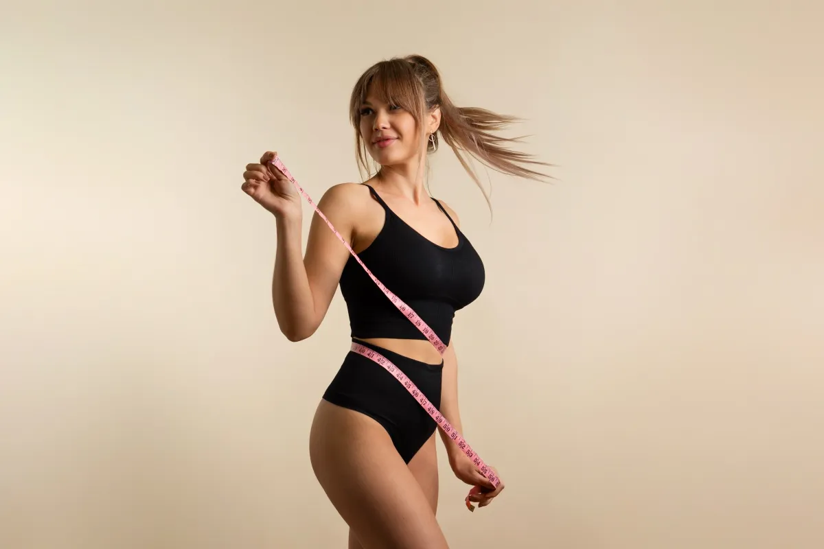 Woman in black activewear holding a pink measuring tape around her waist.