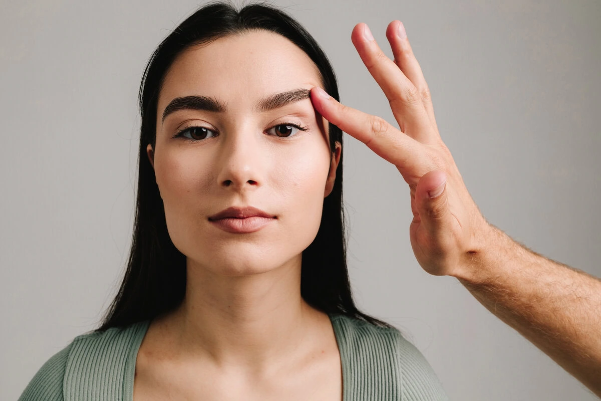 Woman having her eyebrow area examined or treated by someone's hand.