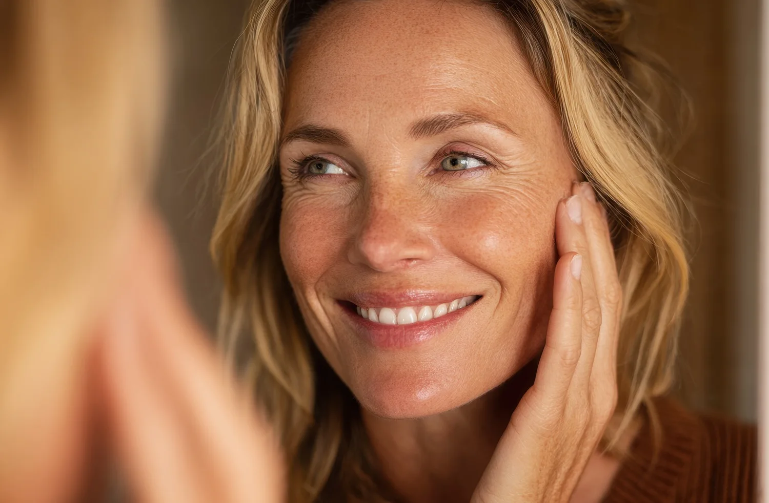 Smiling blonde woman looking in a mirror and touching her face.