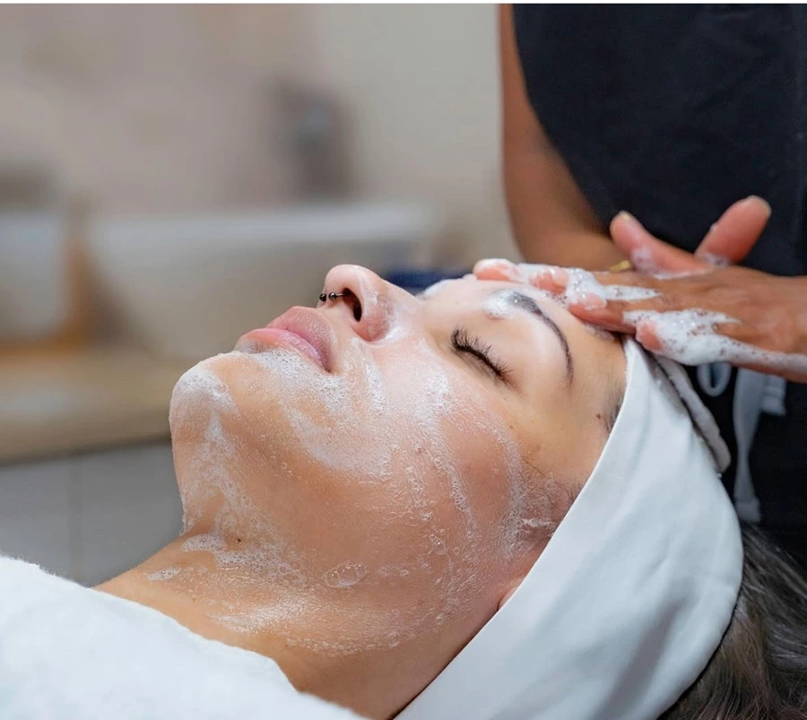 Professional esthetician performing a gentle facial cleansing treatment with foaming cleanser.